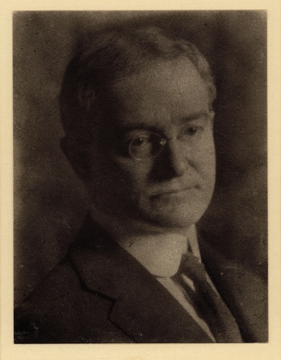 Head shot of man in glasses, coat, and tie