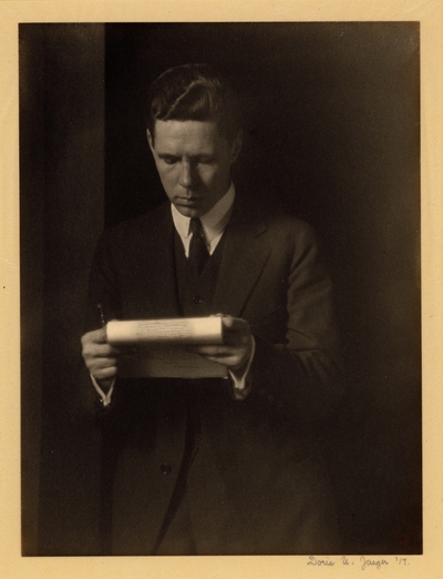 Man in suit and tie, standing with pen and notepad, reading
