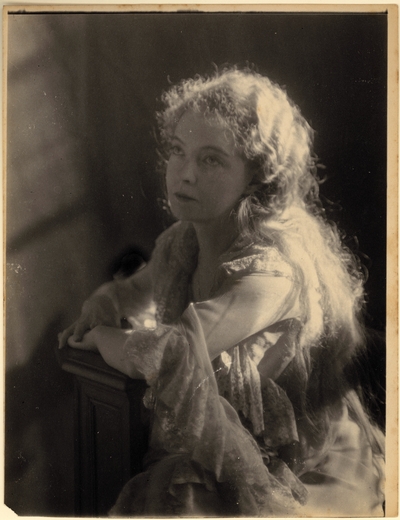 Lillian Gish; Woman with long hair, in lacy costume, seated, leaning on post