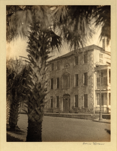 Three-story stone building with porches and columns, palm tree in foreground
