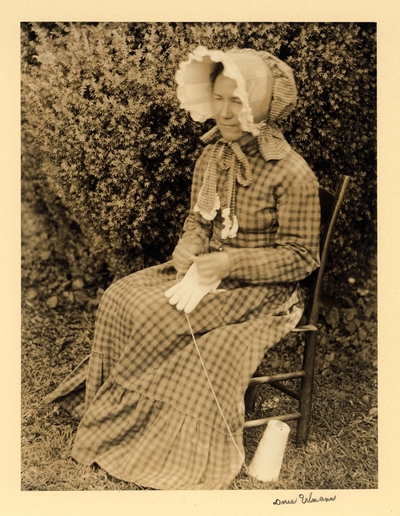 Della S. Cossnell; Woman in long dress and bonnet, seated in chair, tatting gloves