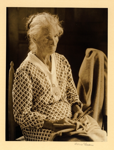 Aunt Lizzie Regan.  Weaver, Gatlinburg, Tenn.  Elderly woman in checked dress, her hair in a bun, seated in chair with fabric and scissors in her lap