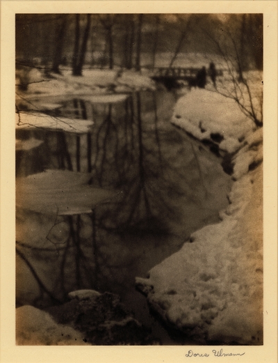 Winter scene with river, snow-covered banks, trees, and bridge in background