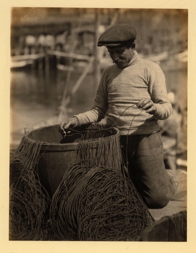 Man with mustache and hat, kneeling beside barrel with lines running into it