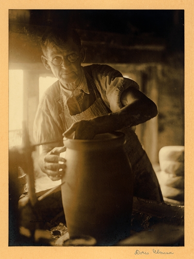 Bybee Corneilson KY.  Man with glasses, apron, and rolled-up sleeves, standing in pottery shop, making large pot