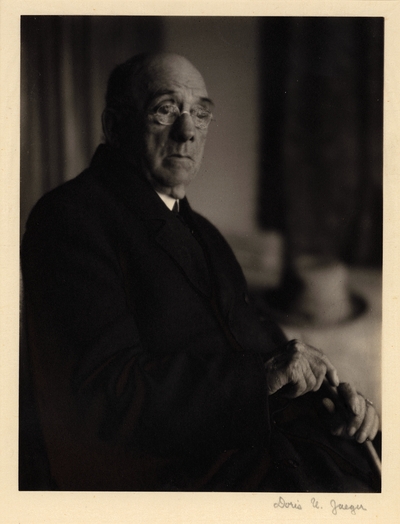 Elderly man in glasses and coat, seated with cane