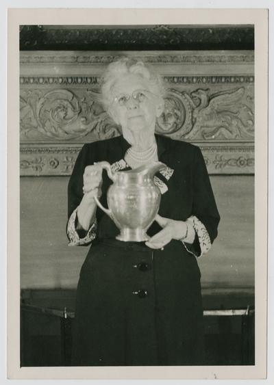 Mrs. George Sprague, widow of Dr. George Sprague, holding the Optimist Club Cup award from Linda Neville