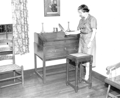 Photograph by the Lexington Herald-Leader an interior view at the Ephraim McDowell House.  An unidentified female is stand next to a writing desk. 8x10