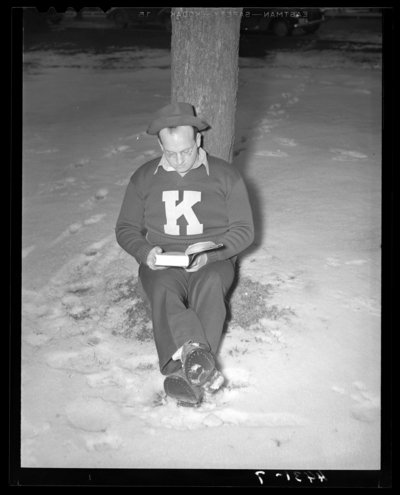 Campus Views (1940 Kentuckian) (University of Kentucky); man                             wearing a University of Kentucky sweater sitting at the base of a tree,                             reading a book