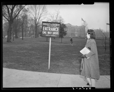 Campus Views, (University of Kentucky); exterior, woman walking                             past a sign reading 