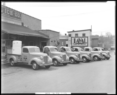 Local Ice Company (Lewis at East Third, 3rd); six company trucks                             parked in front of business, four men standing next to trucks; sign                             painted on building next door reads 