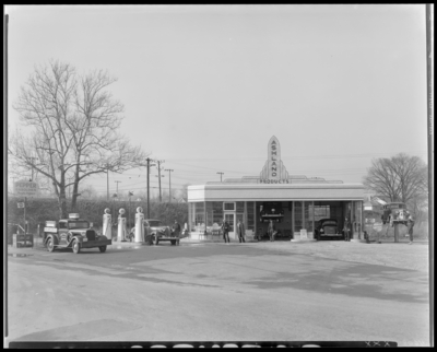 Two Cars Gas Station (service station), (Broadway and Loudon);                             exterior view, men standing in front of building, cars in service bays,                             company truck parked next to gas pumps; signs read 