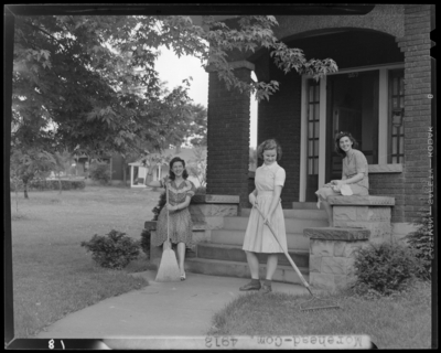 Moorhead College; building, exterior; three women gathered around                             the porch; woman holding a rake; woman holding a broom; woman                             sitting