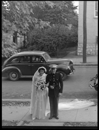 Robinson Wedding (two weddings); West Maple, Nicholasville);                             portrait book; bride and groom standing on the sidewalk for a portrait;                             groom dressed in a uniform; car passing by with onlookers