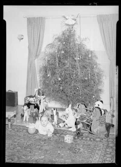 Mrs. W.E. Hupp; interior; baby sitting next to Christmas                             tree