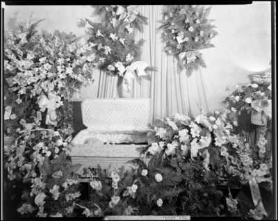 A. H. Woodward; corpse; open casket surrounded by                             flowers
