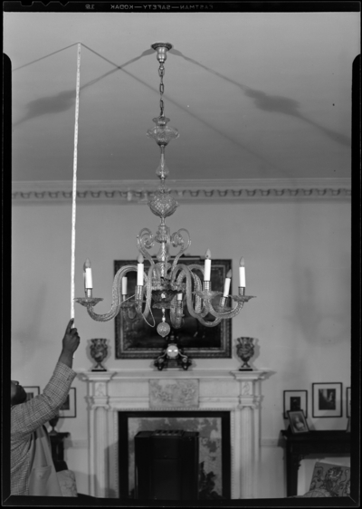 Widener Farm; interior; chandelier hanging in front of fireplace;                             man holding stick up to the ceiling