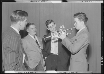 Georgetown College; Alma Ki Alpha; group of three men gathered                             around a fourth playing the horn