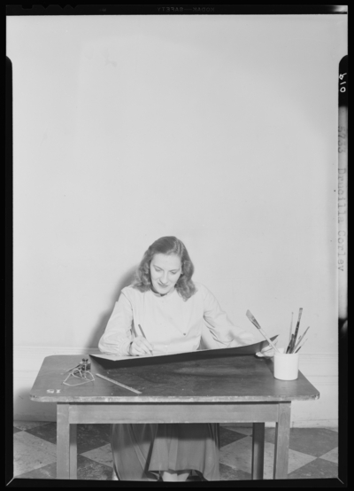 Georgetown College; Drucilla Corley sitting at desk holding                             paintbrush