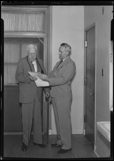 Reverend Mark Collins; interior; two men looking at papers;                             photographs requested by Mutual Life Insurance Company
