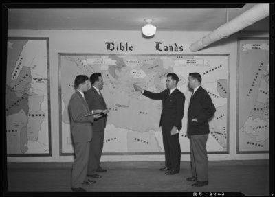 Belle of the Blue; Georgetown College; interior; group of men                             standing in front of wall display for 