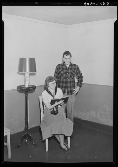 Belle of the Blue; Georgetown College; interior; woman seated in                             a chair holding a book up to a man standing behind her