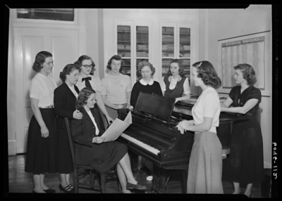 Belle of the Blue; Georgetown College; interior; group of women                             gathered around a piano