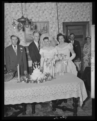 Swindler, Mr. & Mrs.; wedding; interior; bride and groom                             cutting wedding cake; guests standing next to bride and                             groom