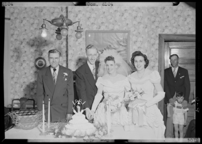 Swindler, Mr. & Mrs.; wedding; interior; bride and groom                             cutting wedding cake; guests standing next to bride and                             groom