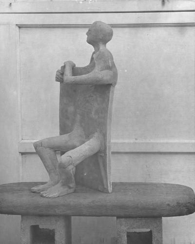 The front of a ceramic sculpture, a human form mixed with a chair shape, by John Tuska