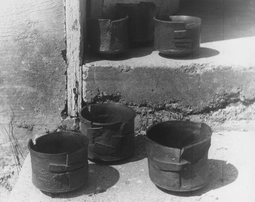Six ceramic slab pots by John Tuska. Round shaped pots formed by slabs of clay bound together by another slab of clay. The pots are sitting on concrete steps. These are the same pots as in image 22