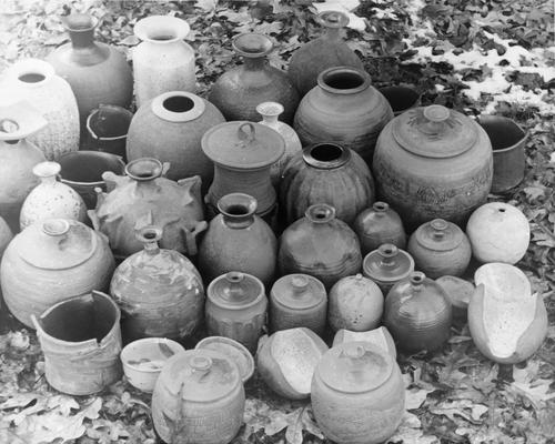 Forty ceramic pots sitting outside in some leaves by John Tuska