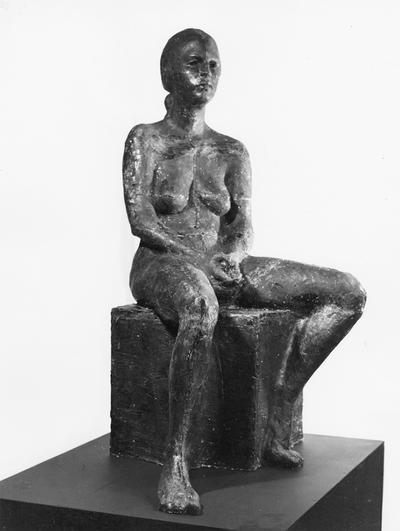 A fiberglass life size sculpture of a female nude sitting on a square by John Tuska. The model's name is Pat