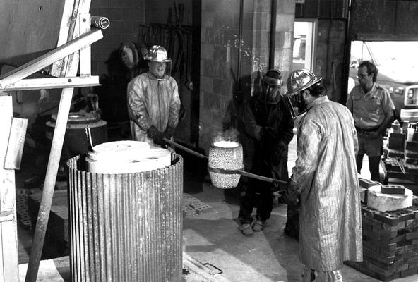 An unidentified man and Jack Gron carrying bronze in a crucible to pour in the mold for the John Sherman Cooper bust. There are other unidentified men standing in this print