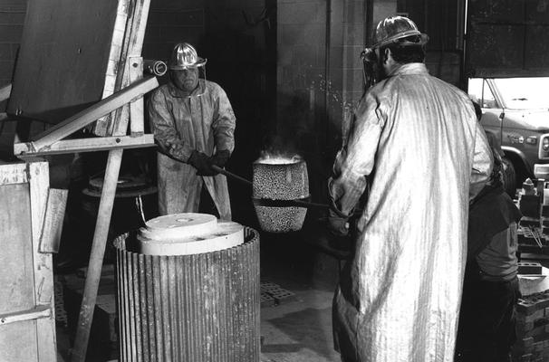 An unidentified man and Jack Gron carrying bronze in a crucible to pour in the mold for the John Sherman Cooper bust