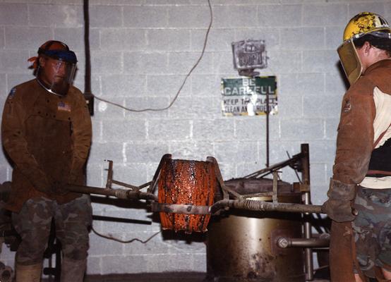 Andrew Marsh and Scott Oberlink lifting a crucible in the University of Kentucky foundry for the casting 