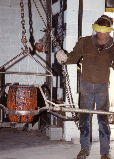 An unidentified man helping to lift a crucible in the University of Kentucky foundry for the casting 