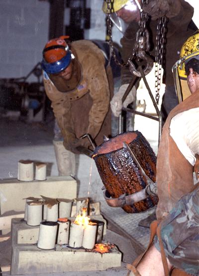 Scott Oberlink, an unidentified man and Andrew Marsh pouring bronze from a crucible in the University of Kentucky foundry for the casting 