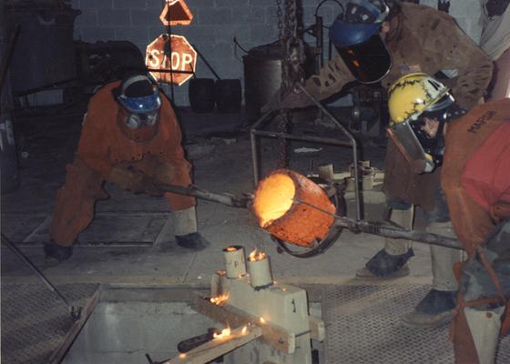 An unidentified man, Scott Oberlink and Andrew Marsh pouring bronze in the University of Kentucky foundry for 