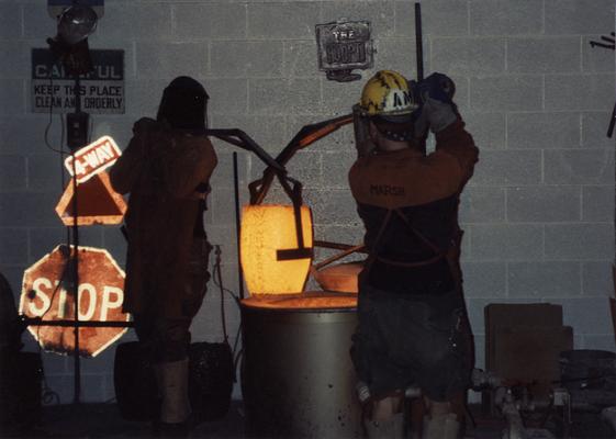 Scott Oberlink and Andrew Marsh lifting a crucible out of the furnace in the University of Kentucky foundry for the casting of 