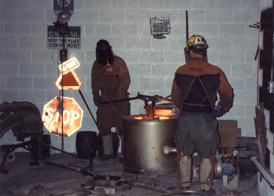 Scott Oberlink and Andrew Marsh lifting a crucible out of the furnace to pour bronze in the University of Kentucky foundry for the casting of 