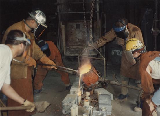 An unidentified man, Jack Gron, an unidentified man, Scott Oberlink and Andrew Marsh pouring bronze in the University of Kentucky foundry for the casting of 