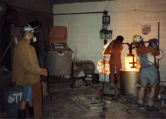 Jack Gron, an unidentified man and Andrew Marsh lifting a crucible out of the furnace in the University of Kentucky foundry for the casting of 