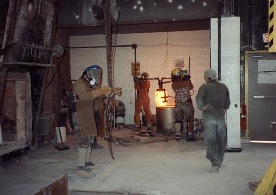 Scott Oberlink, an unidentified man, Andrew Marsh and an unidentified man lifting a crucible out of the furnace in the University of Kentucky foundry for the casting of 