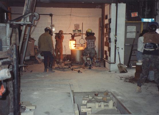 Jack Gron, an unidentified man, Andrew Marsh and Scott Oberlink lifting a crucible out of the furnace in the University of Kentucky foundry for the casting of 