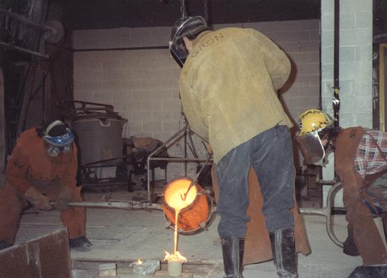 An unidentified man, Jack Gron and Andrew Marsh pouring bronze in the University of Kentucky foundry for the casting of 