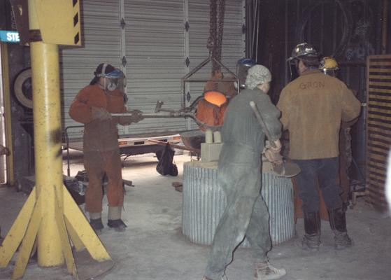 An unidentified man, Scott Oberlink, an unidentified man, Jack Gron and Andrew Marsh pouring bronze in the University of Kentucky foundry for the casting of 