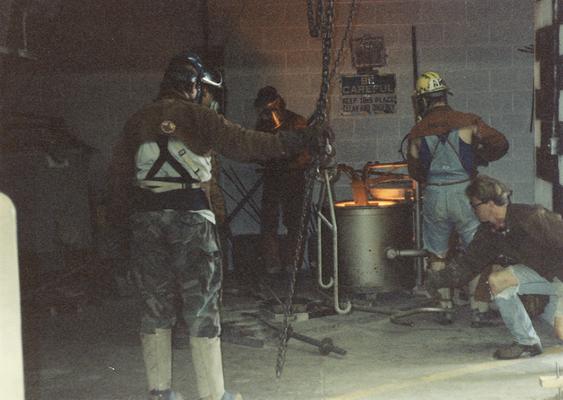 Scott Oberlink, an unidentified man, Andrew Marsh and an unidentified man lifting a crucible out of the furnace in the University of Kentucky foundry for the casting of 