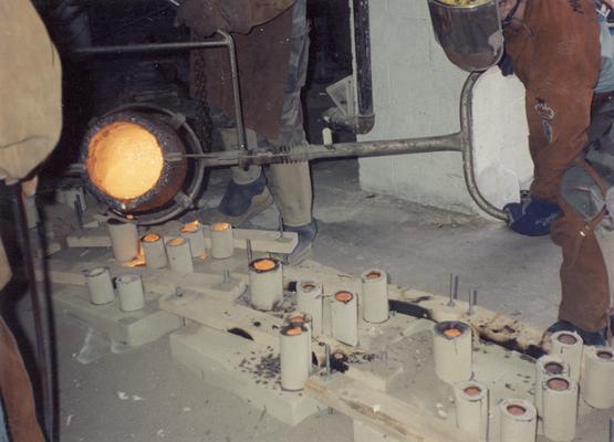 An unidentified man, Scott Oberlink and Andrew Marsh pouring bronze in the University of Kentucky foundry for the casting of 
