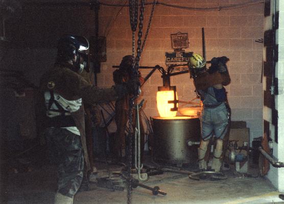 Scott Oberlink, Jack Gron, an unidentified man and Andrew Marsh lifting a crucible out of the furnace in the University of Kentucky foundry for the casting of 